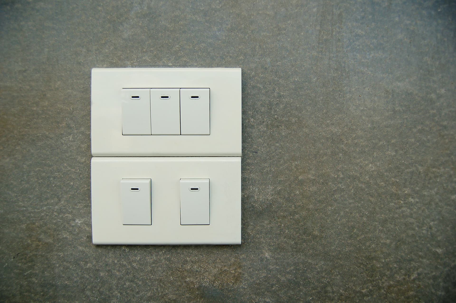 A close view of a row of white rocker switches mounted flush on a pale textured wall.